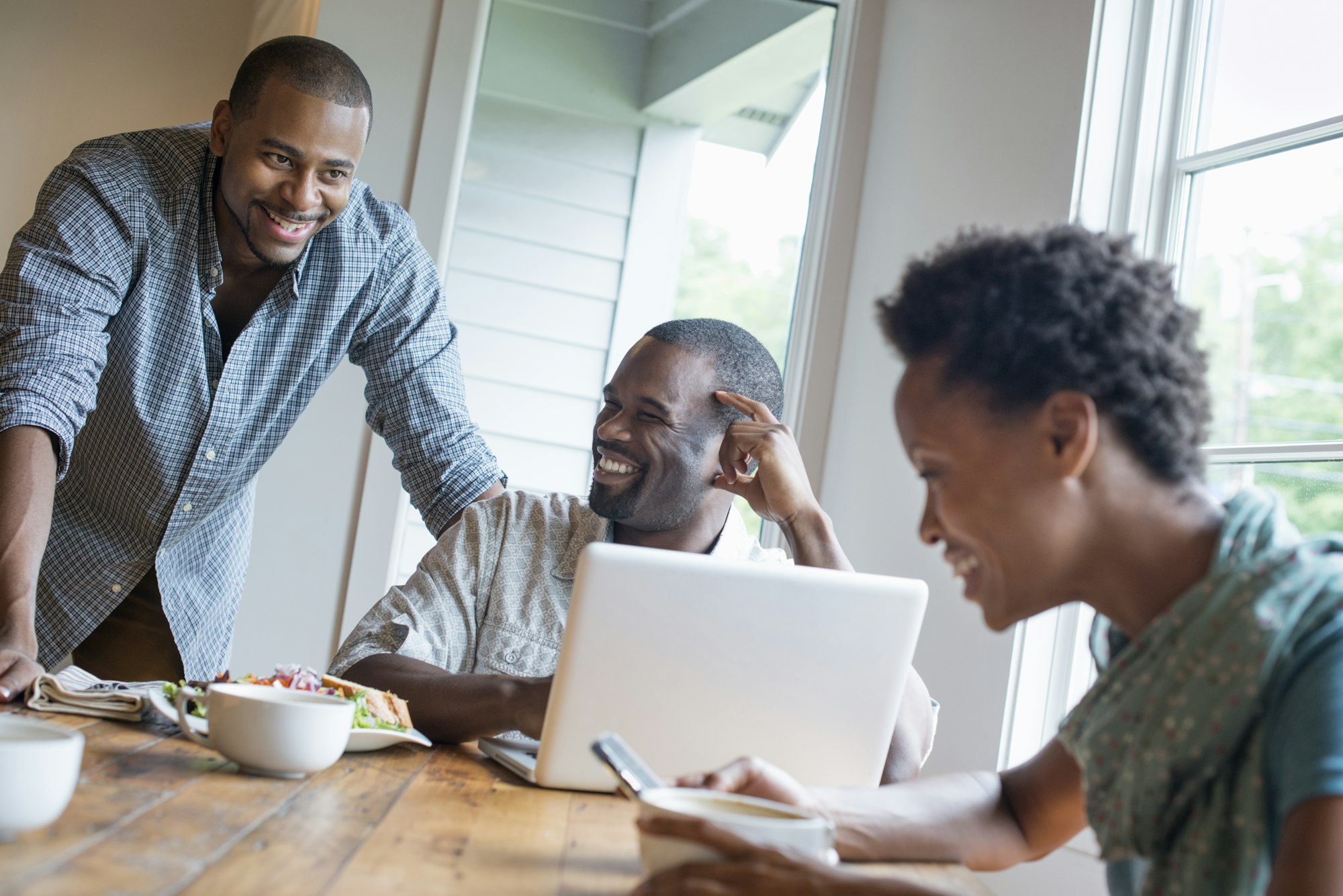 A group of three people in a cafe. Sharing a laptop and using smart phones.