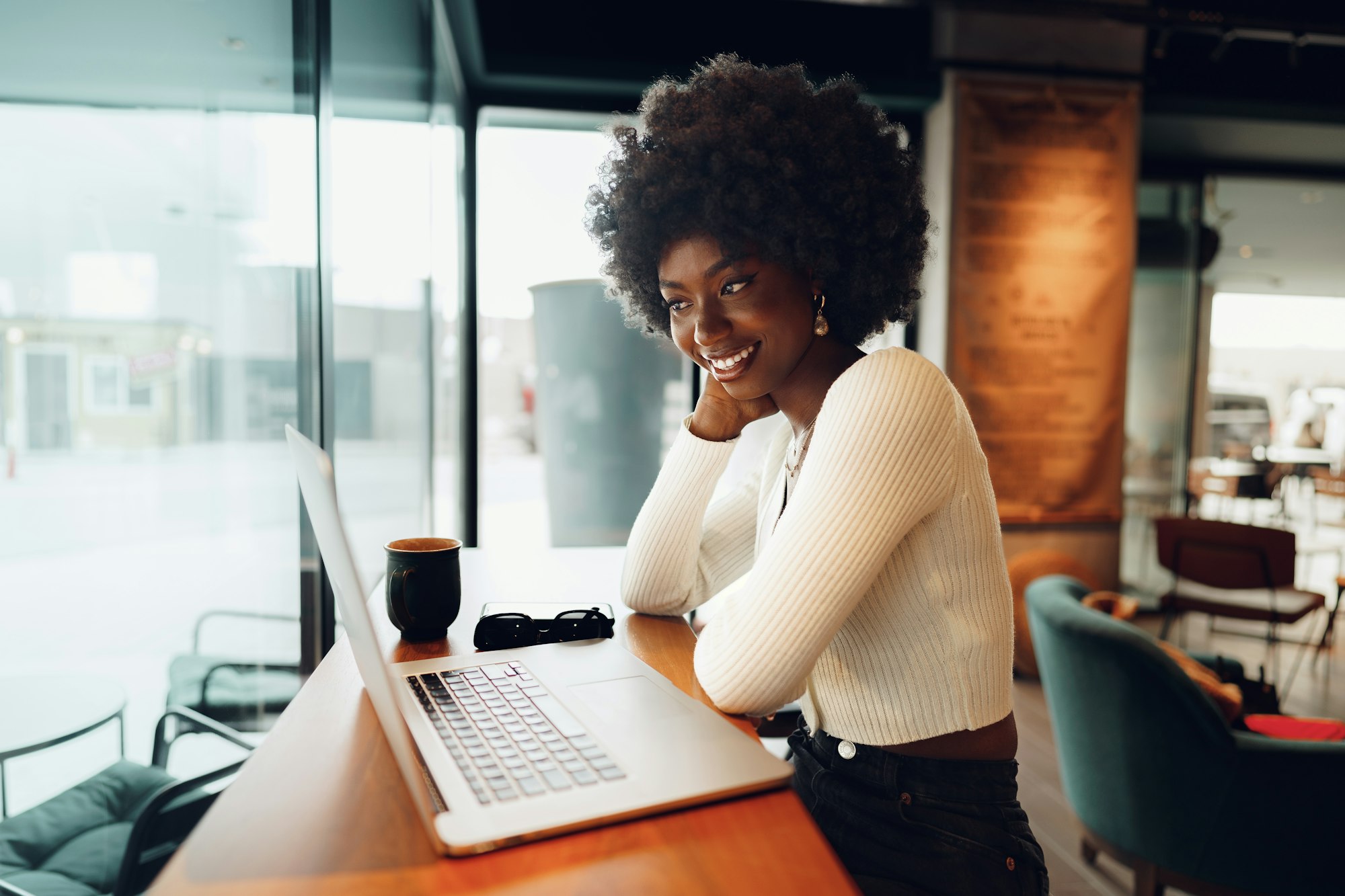 Smiling young african woman sitting with laptop in cafe